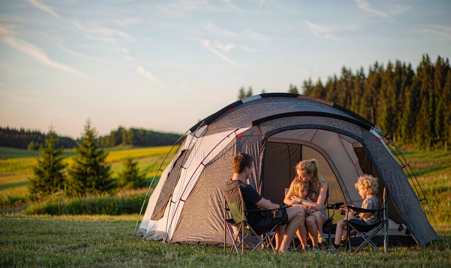 Family relaxing outside a large dome camping tent in a meadow at sunset