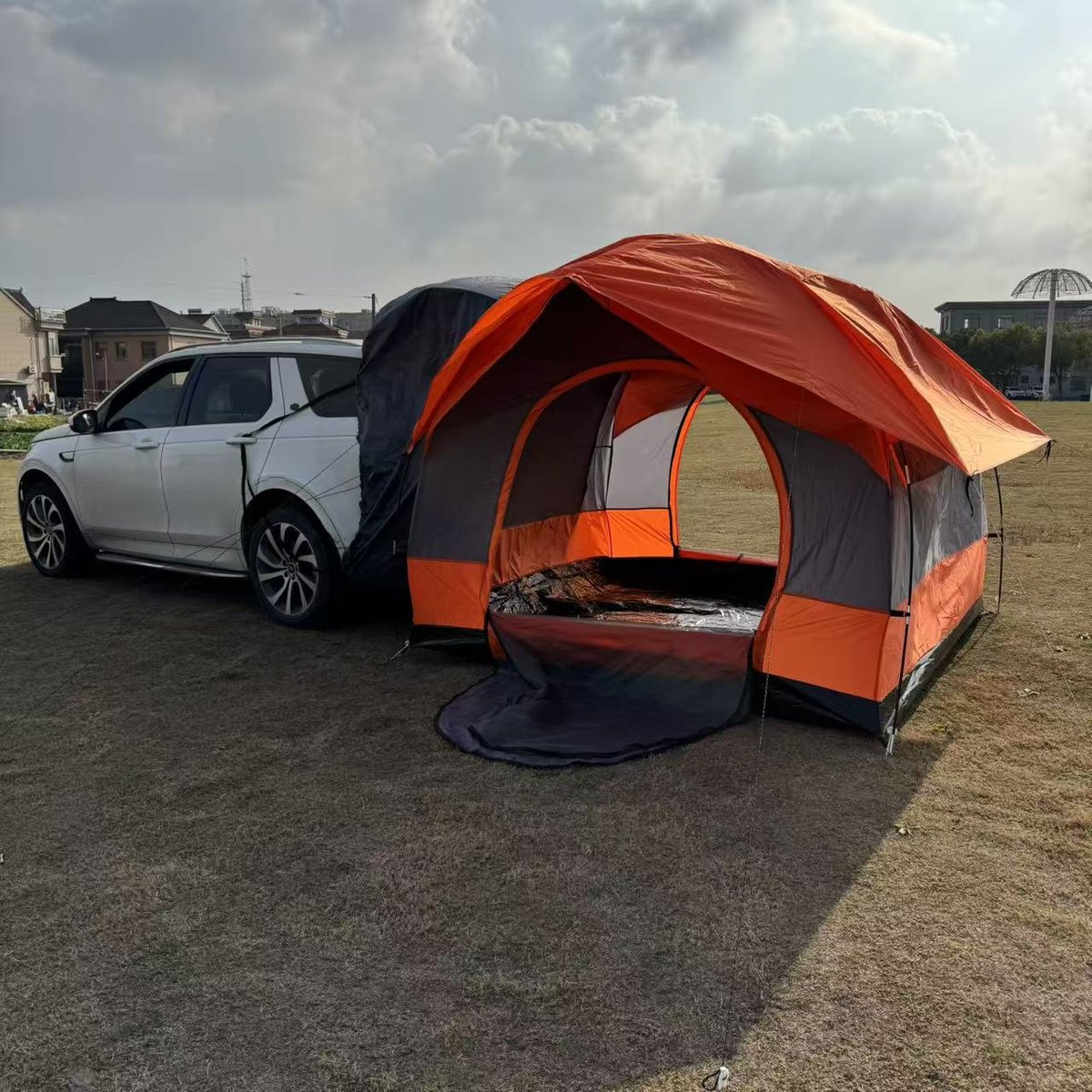 Double-layer tailgate tent in orange and grey attached to the rear of an SUV on grass — Armand Outdoor wholesale